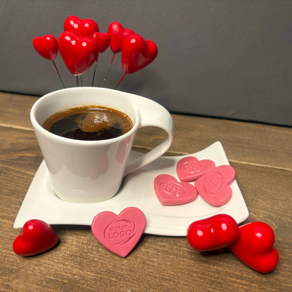 Pink heart-shaped chocolates with a custom logo displayed beside a cup of coffee