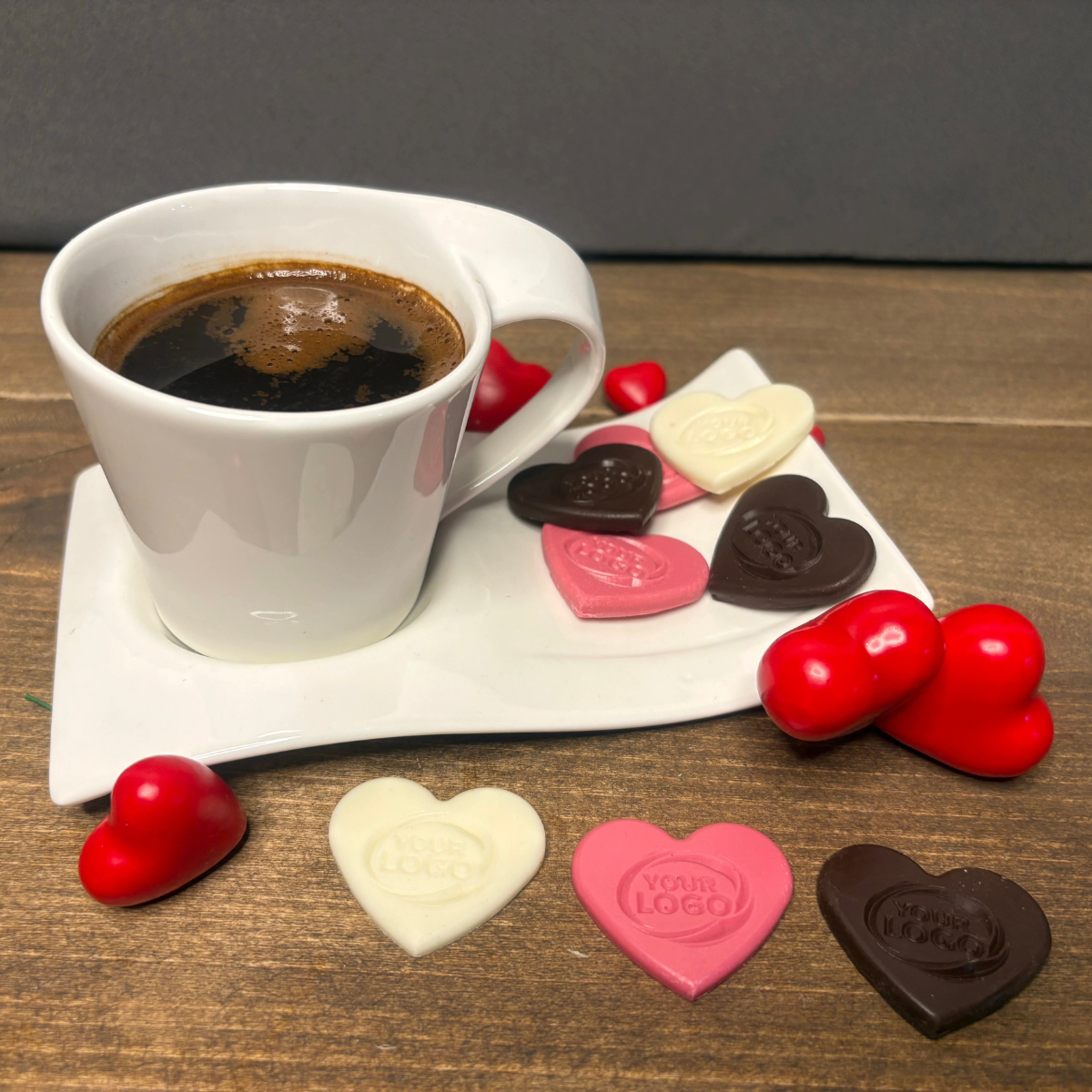 Custom heart-shaped chocolates with logo displayed next to a cup of coffee in dark, white and pink chocolate